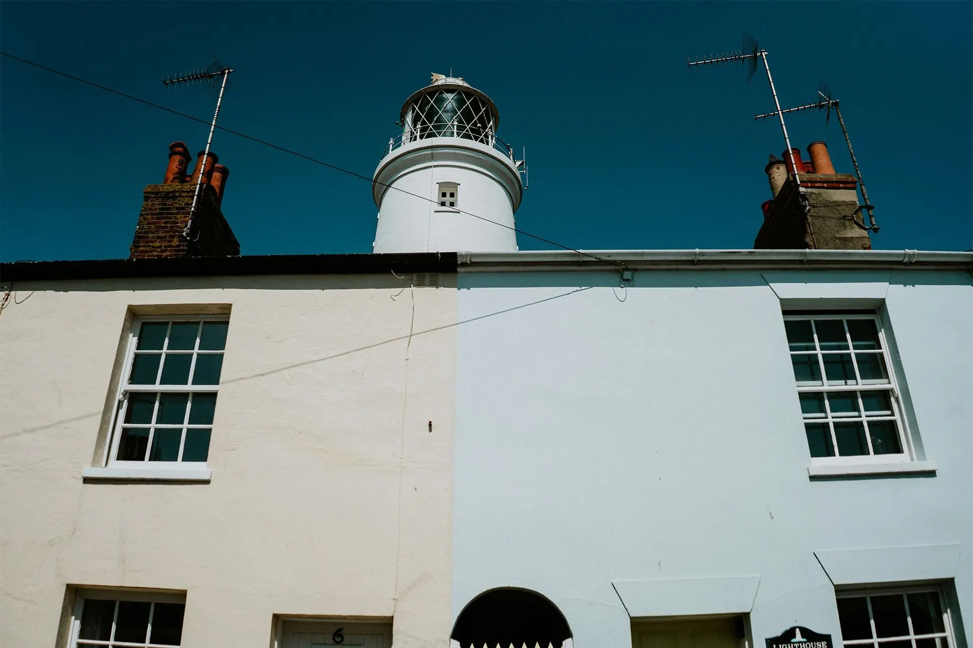 White lighthouse above a row of houses against a blue sky.