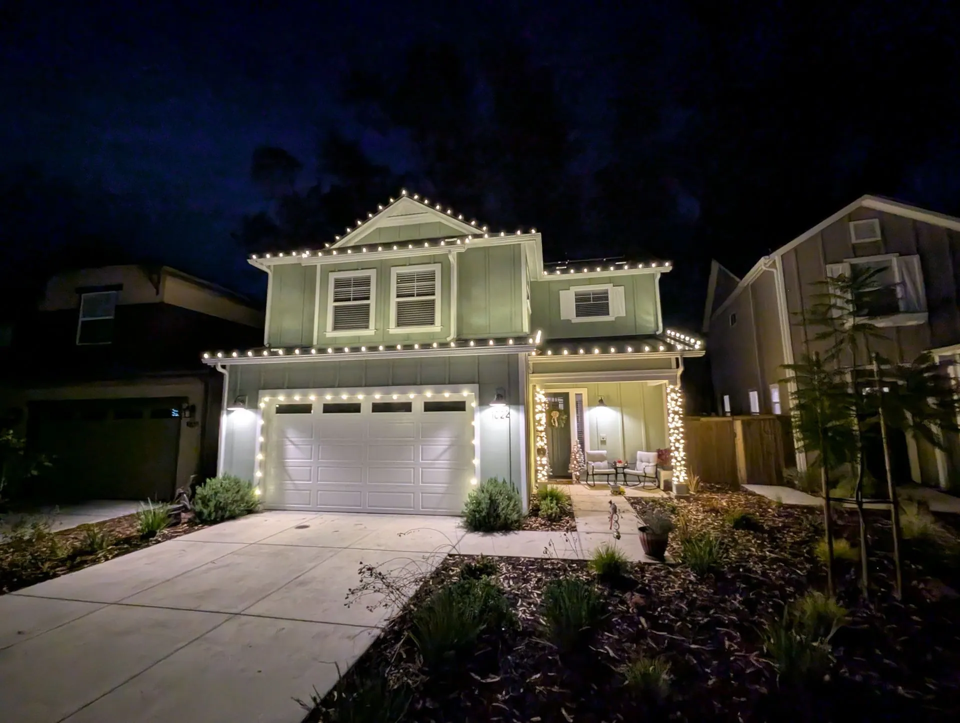 Two-story home with warm white Christmas lights along the rooflines, garage and porch, installed by Clear Wave Windows